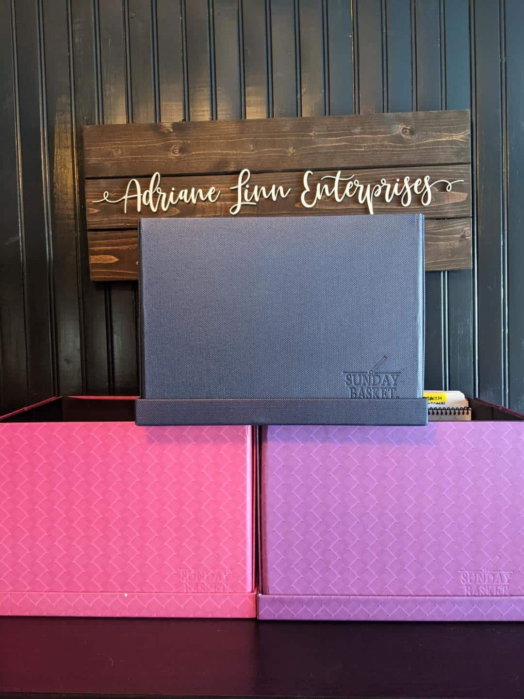 Three Sunday Basket® boxes stacked below an Adriane Linn Enterprises sign